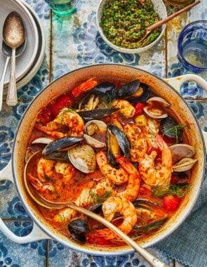 a dutch oven with cioppino ingredients including fennel, onion, roasted red peppers, oregano and thyme.