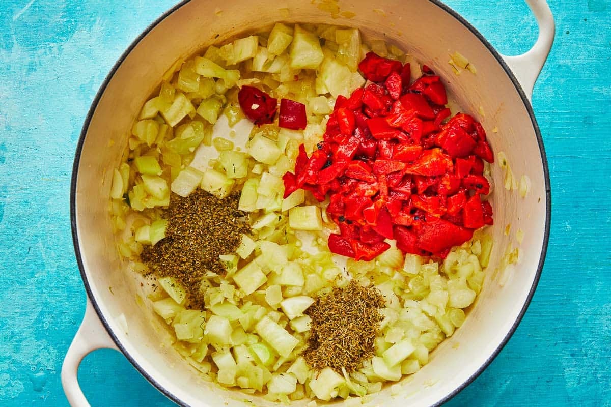 a dutch oven with cioppino ingredients including fennel, onion, roasted red peppers, oregano and thyme.