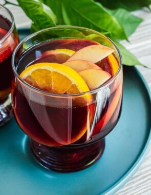 close up of a glass of red sangria with sliced apples and oranges.