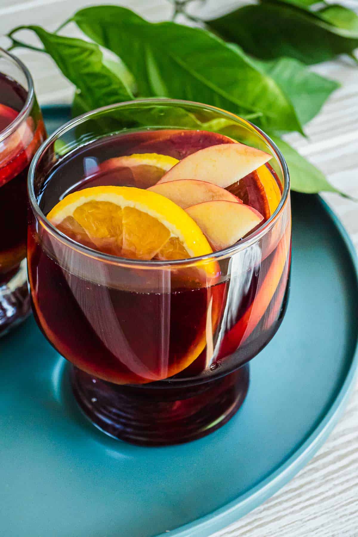 close up of a glass of red sangria with sliced apples and oranges.
