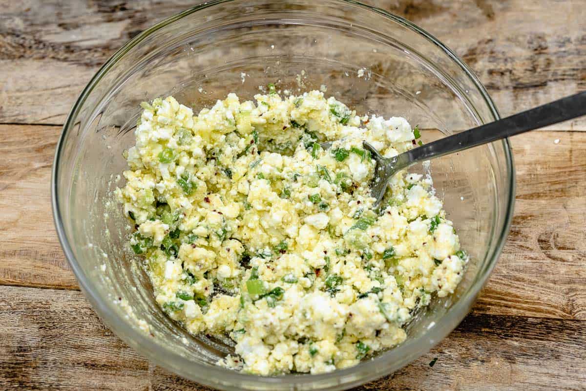 sigara boregi filling of feta cheese, parmesan cheese, scallions, parsley, thyme and red pepper flakes in a glass bowl with a spoon.