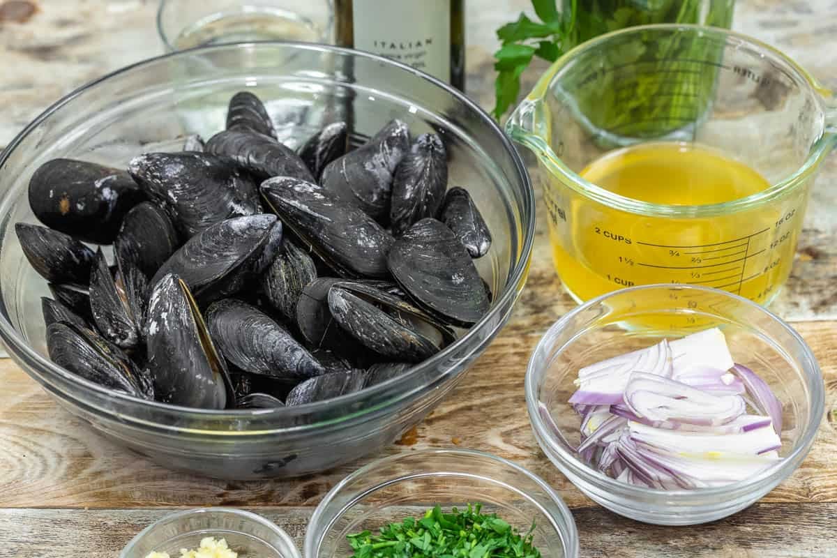 Ingredients for steamed mussels including mussels, olive oil, vegetable broth, white wine, shallots, garlic and parsley.