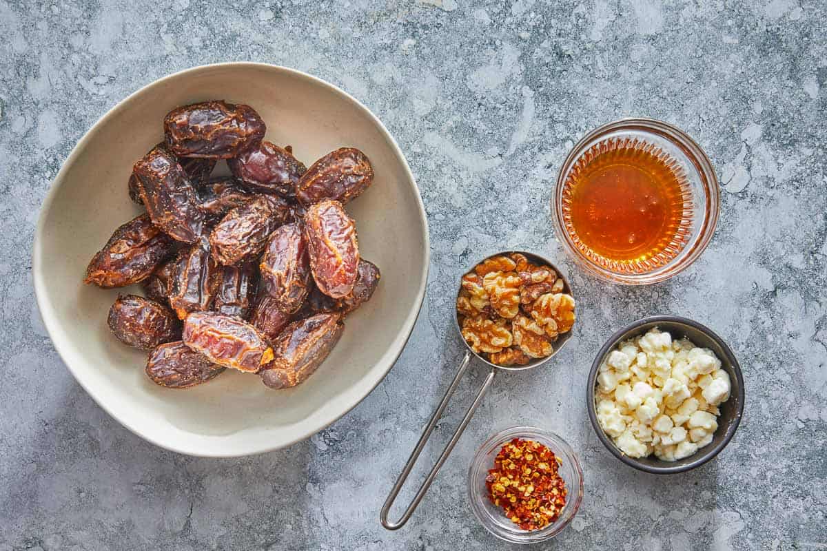 ingredients for stuffed dates including dates, walnuts, red pepper flakes, honey and goat cheese.