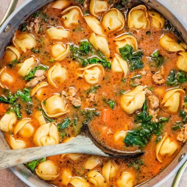tortelllini soup in a dutch oven with a wooden spoon.