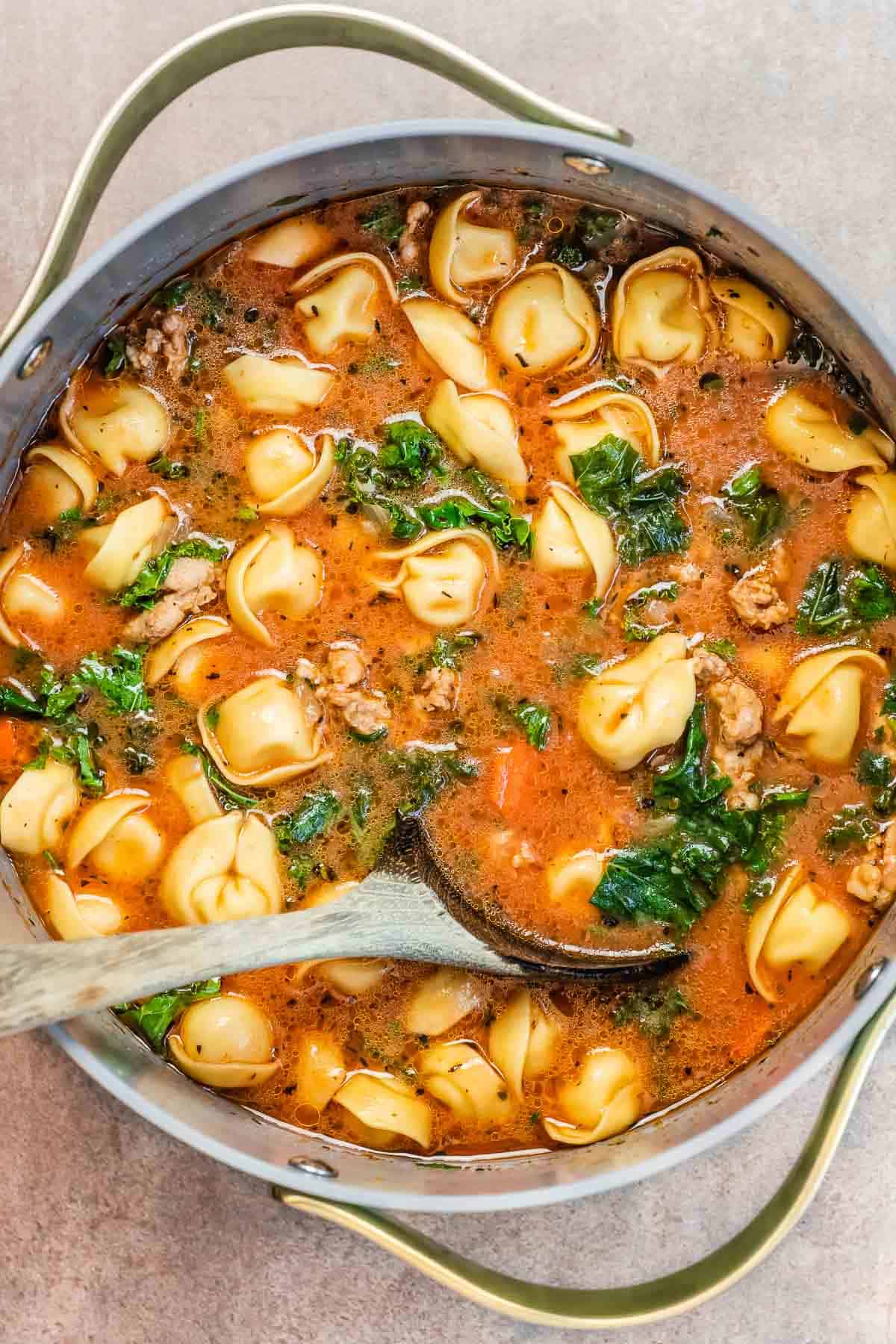 tortelllini soup in a dutch oven with a wooden spoon.