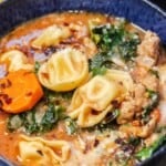 close up of tortellini soup in a blue bowl.