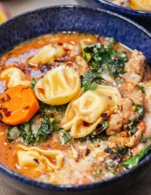 close up of tortellini soup in a blue bowl.