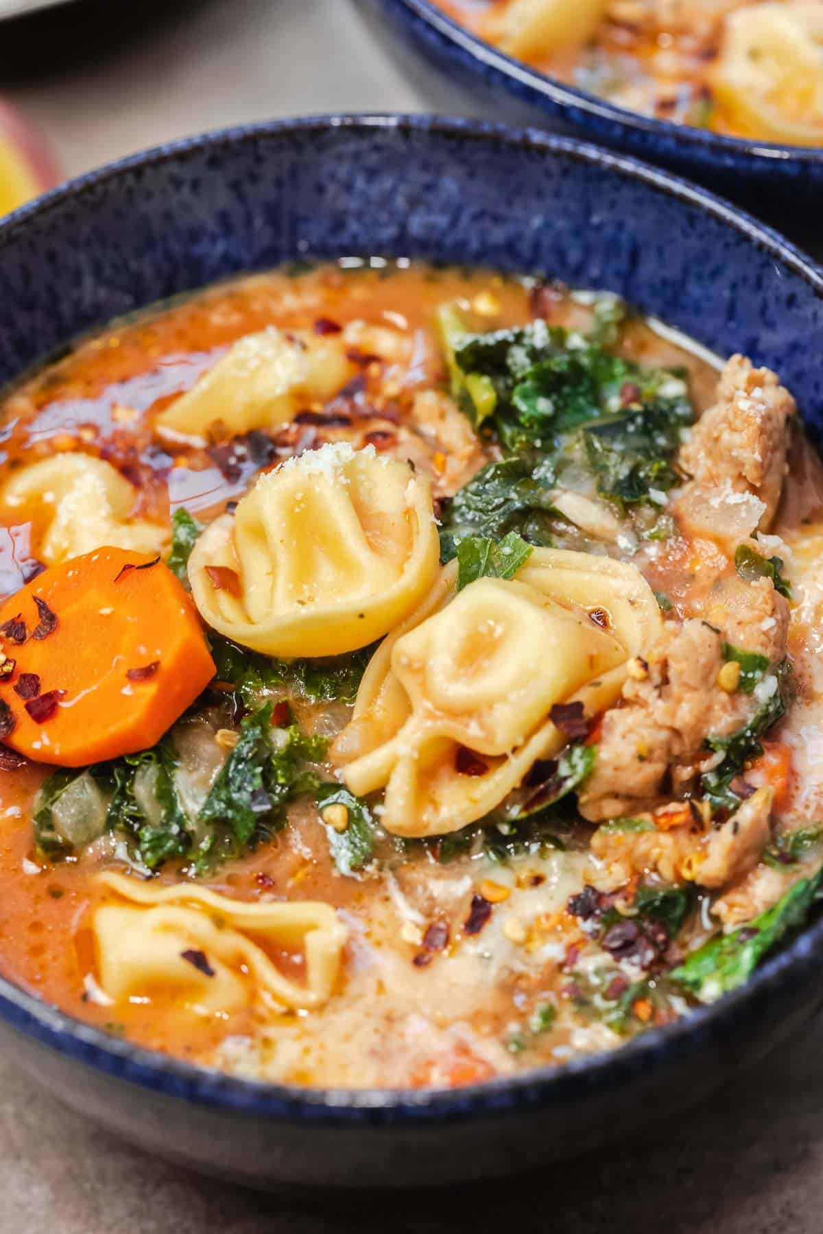 close up of tortellini soup in a blue bowl.