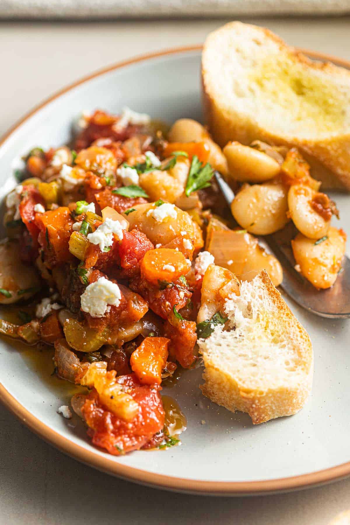 slices of bread topped with Greek baked white beans (gigantes plaki) on a plate with a fork.