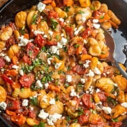 close up of cooked gigantes plaki in a cast iron skillet with a spoon.