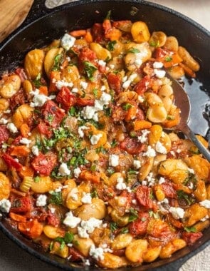 close up of cooked gigantes plaki in a cast iron skillet with a spoon.