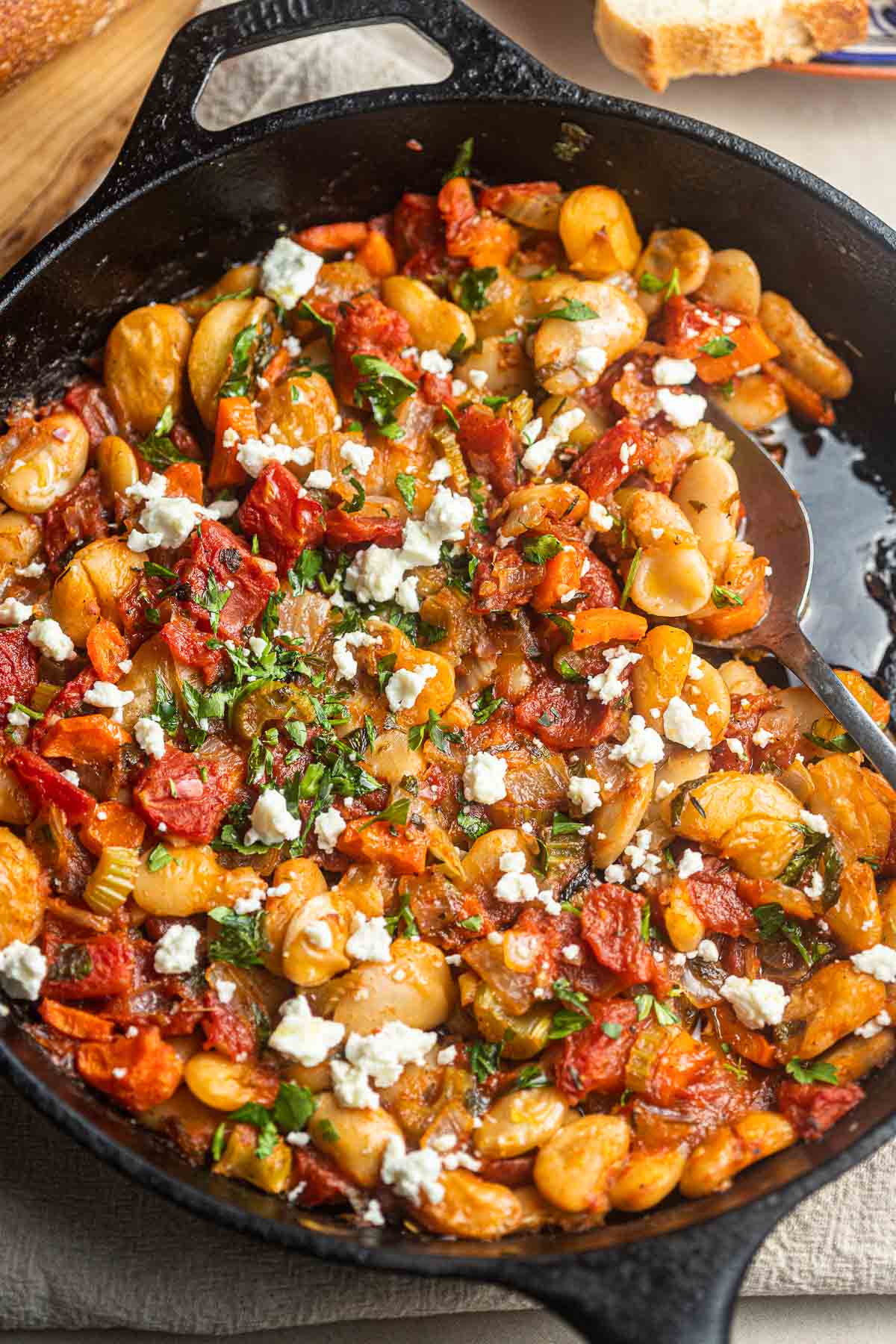 close up of cooked Greek baked white beans (gigantes plaki) in a cast iron skillet with a spoon.