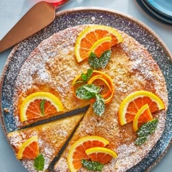 orange cardamom olive oil cake one a plate topped with orange slices with one slice cut.