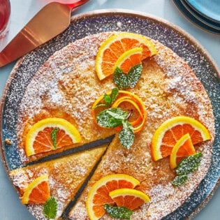 orange cardamom olive oil cake topped with orange slices on a plate with one slice cut.