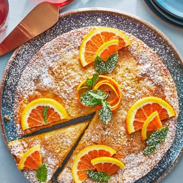 orange cardamom olive oil cake topped with orange slices on a plate with one slice cut.