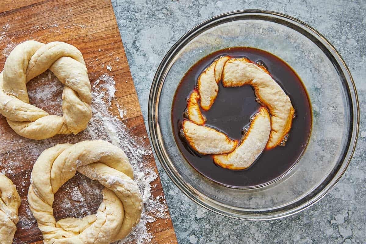 a simit dough ring being dipped into the molasses mixture.