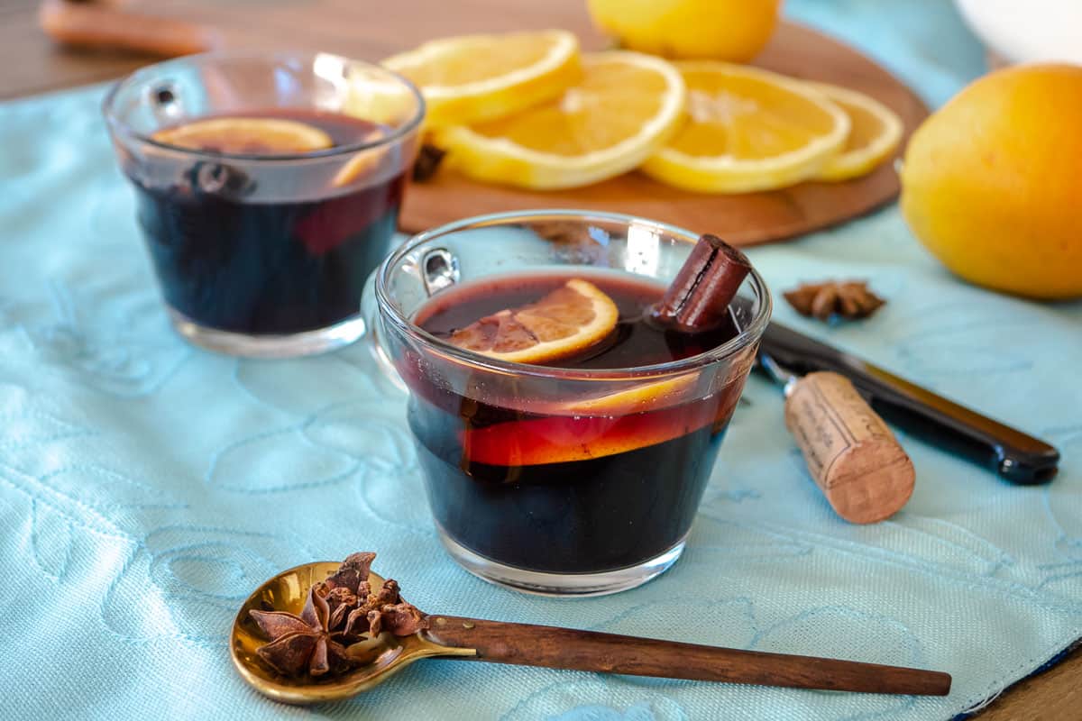 two cups of mulled wine with orange slices and cinnamon sticks.