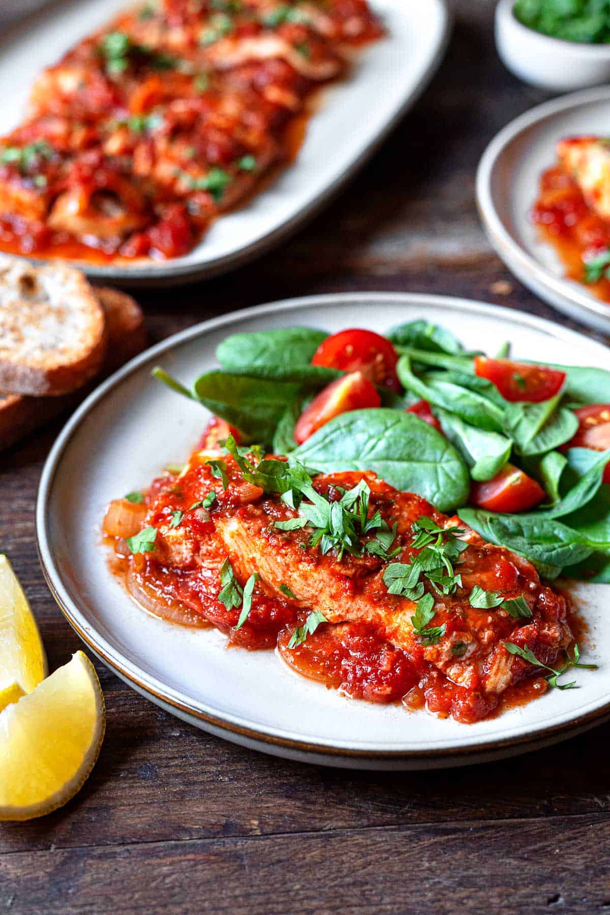 greek fish with onions and tomato on a plate with a spinach salad with tomatoes.