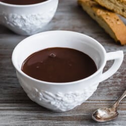 a close up of a mug of hot chocolate next to a spoon and two slices of biscotti.