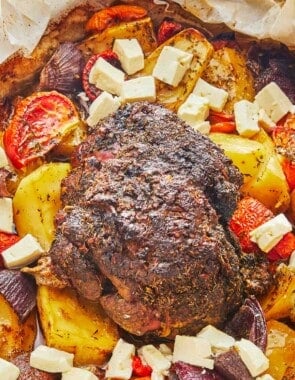 lamb kleftiko, vegetables and chunks of feta in a roasting pan lined with parchment paper.