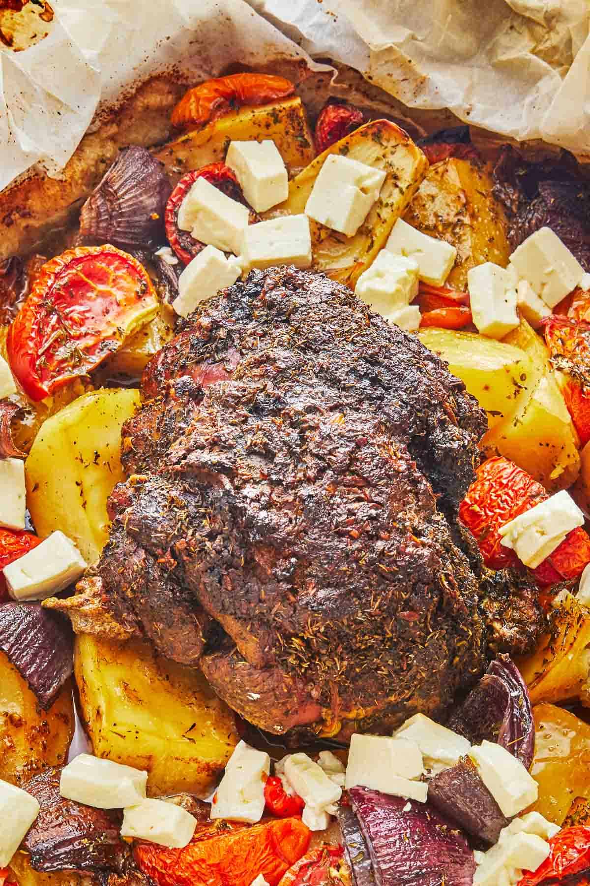 lamb kleftiko, vegetables and chunks of feta in a roasting pan lined with parchment paper.