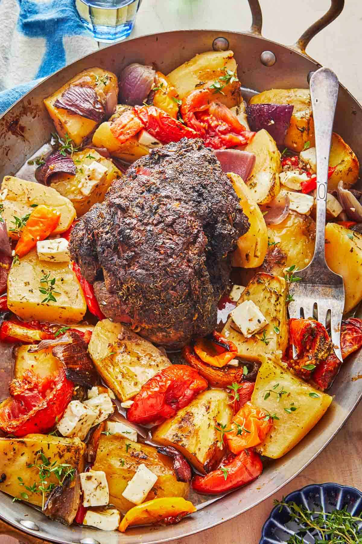 lamb kleftiko and vegetables in a roasting pan with a serving fork.