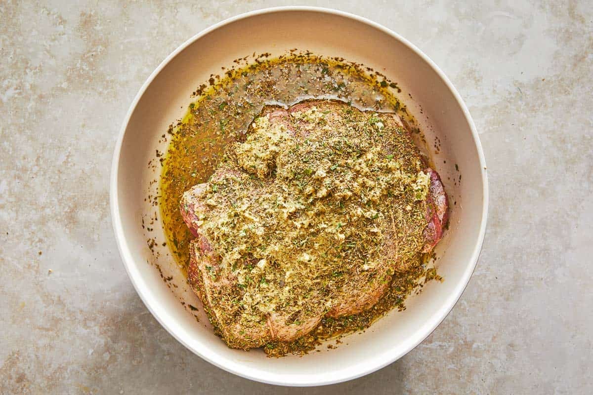 uncooked boneless leg of lamb marinating in a bowl.