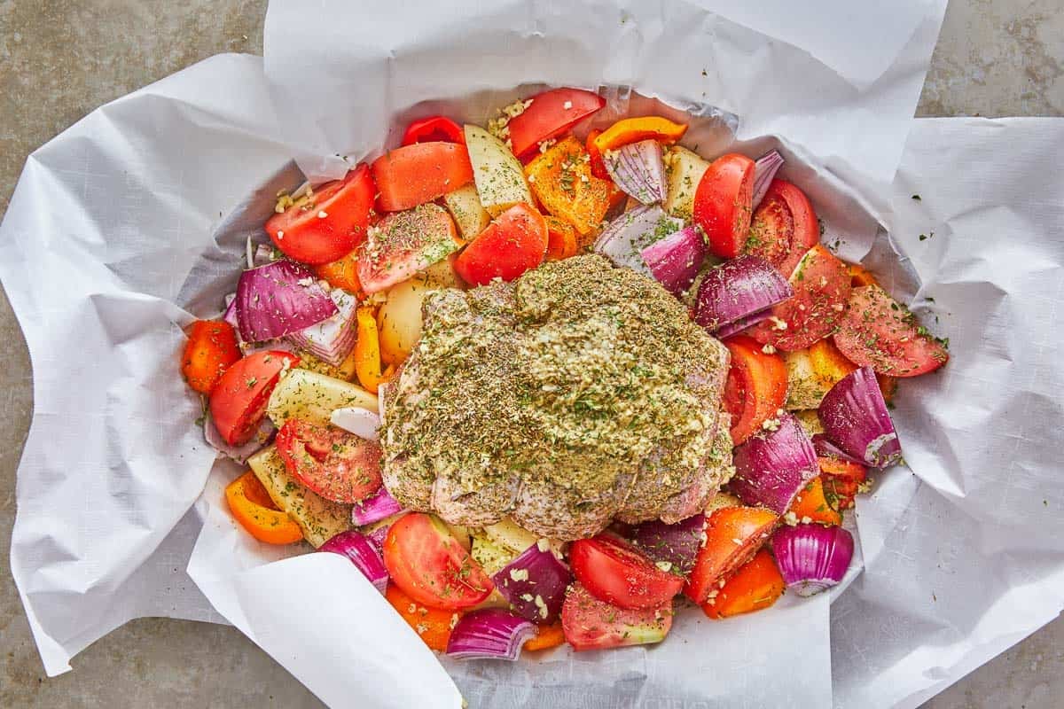 uncooked lamb kleftiko and vegetables in a roasting pan lined with parchment paper.