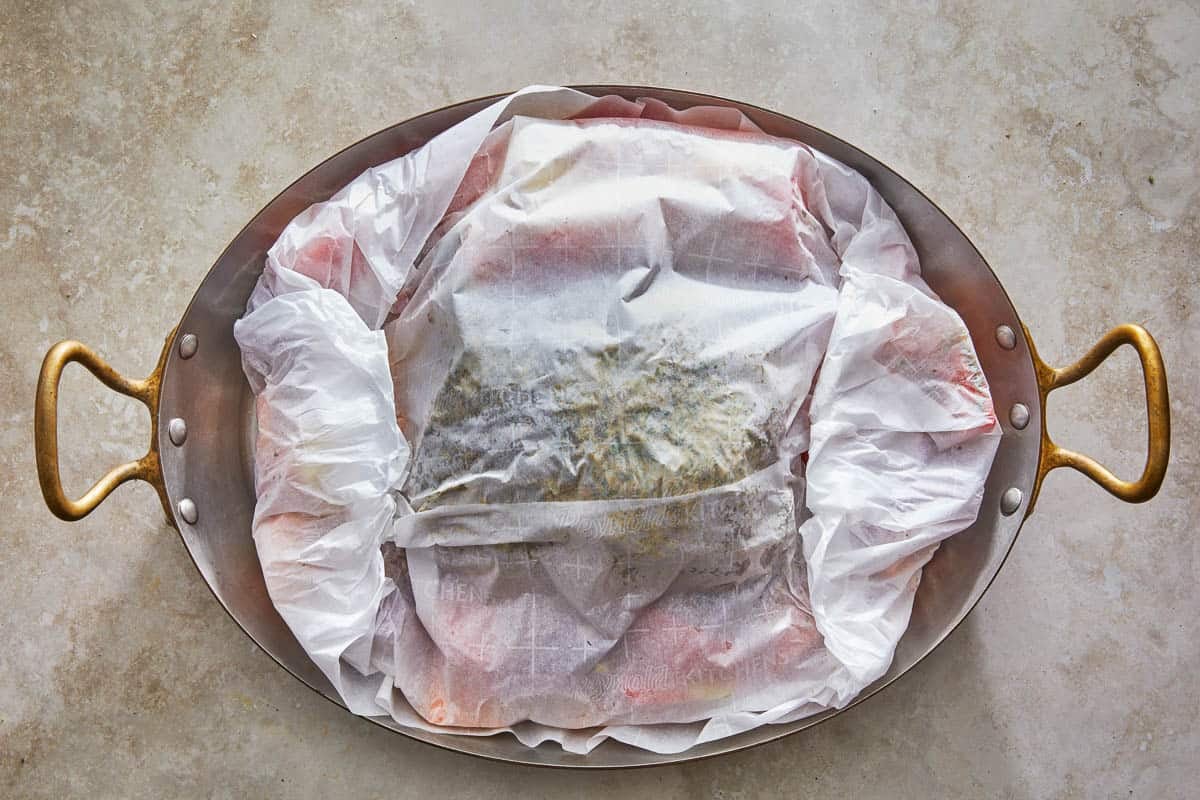 lamb kleftiko and vegetables wrapped in parchment paper in a roasting pan.