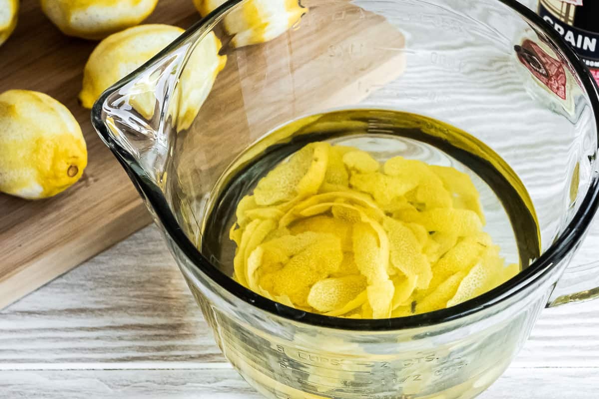 lemon peels in a glass bowl with lemons in the background.