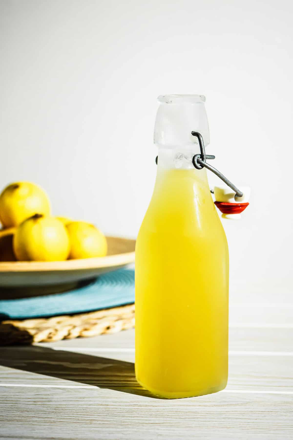 A bottle of limoncello with a bowl of lemons in the background.