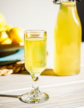 a glass of limoncello with a bottle of limoncello in the background.