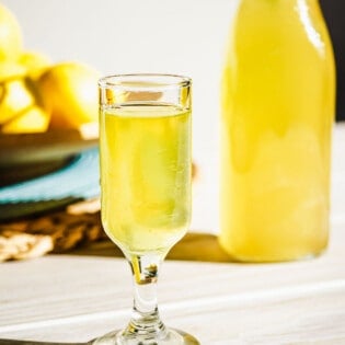 a glass of limoncello with a bottle of limoncello in the background.