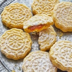 close up of six whole and one broken ma'amoul cookies on a plate.