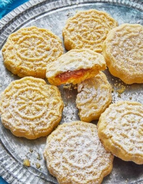 close up of six whole and one broken ma'amoul cookies on a plate.