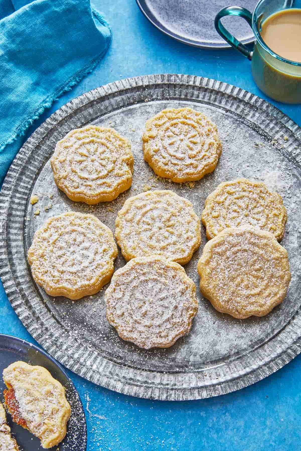 seven ma'amoul cookies sprinkled with confectioners' sugar on a plate.