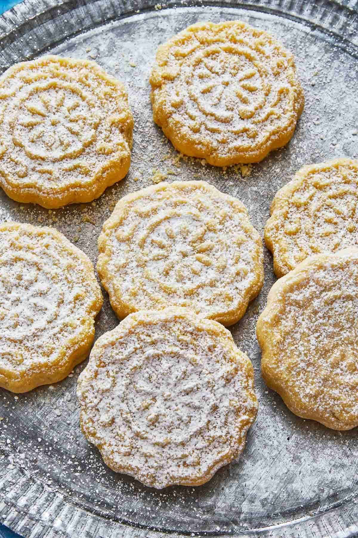 close up of seven ma'amoul cookies sprinkled with confectioners' sugar on a plate.