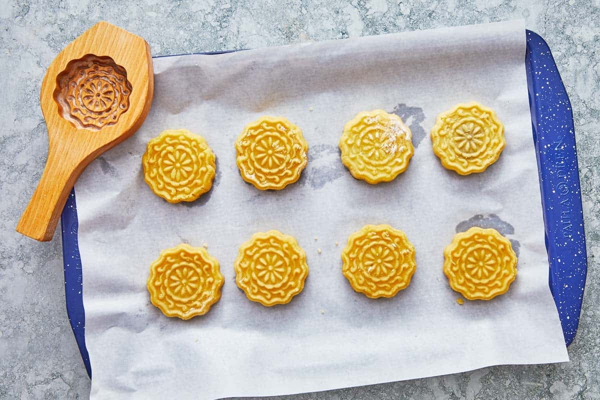 eight uncooked ma'amoul cookies on baking sheet lined with parchment paper with a cookie mold in the background..