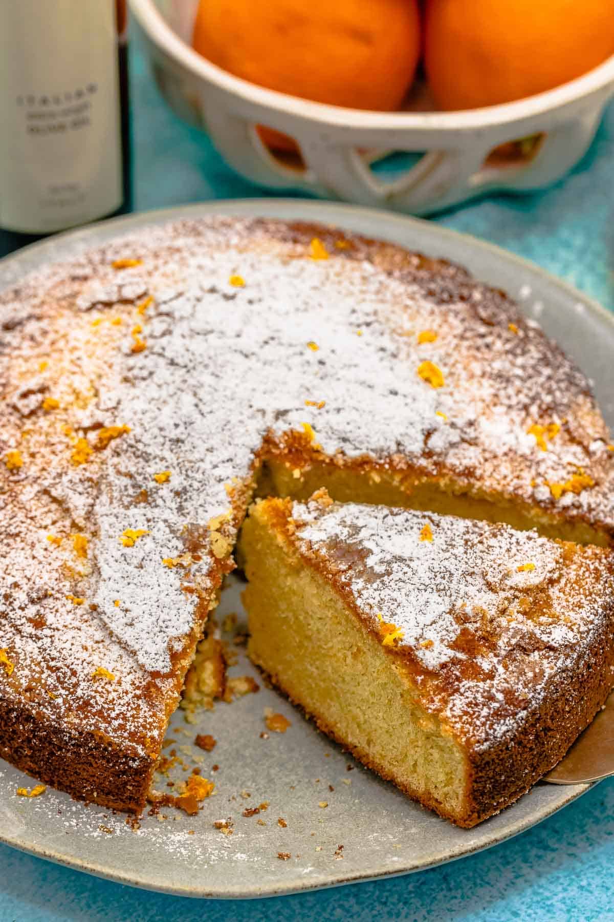 close up of an orange cardamom olive oil cake on a plate with one slice cut.