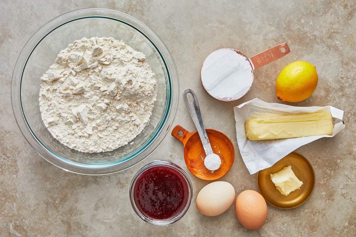 Ingredients for pizzicati cookies including flour, powdered sugar, a lemon, butter, baking powder, two eggs and strawberry jam.