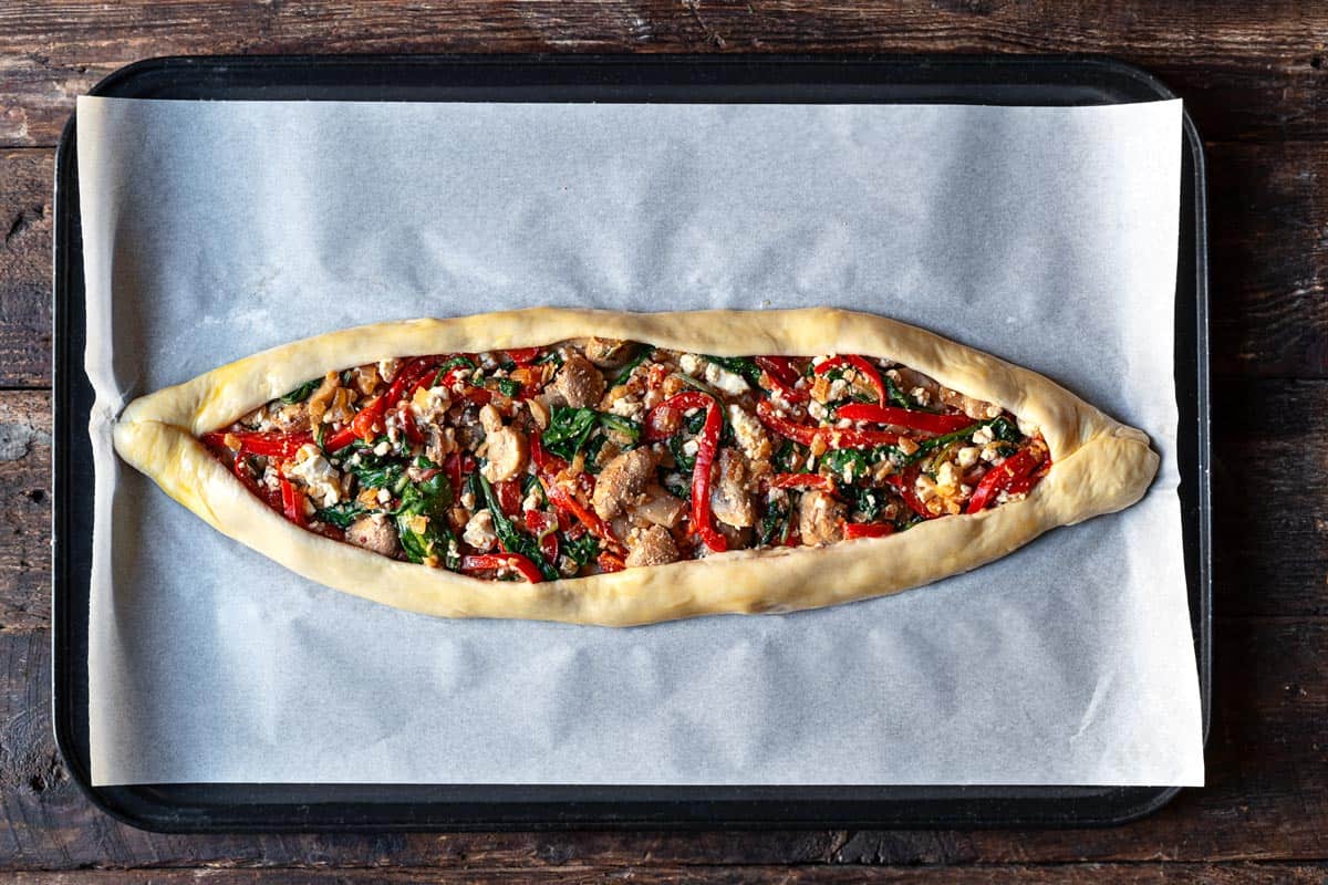 unbaked vegetarian turkish pide on a parchment paper line baking sheet.