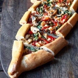 one vegetarian turkish pide sliced on a serving board.