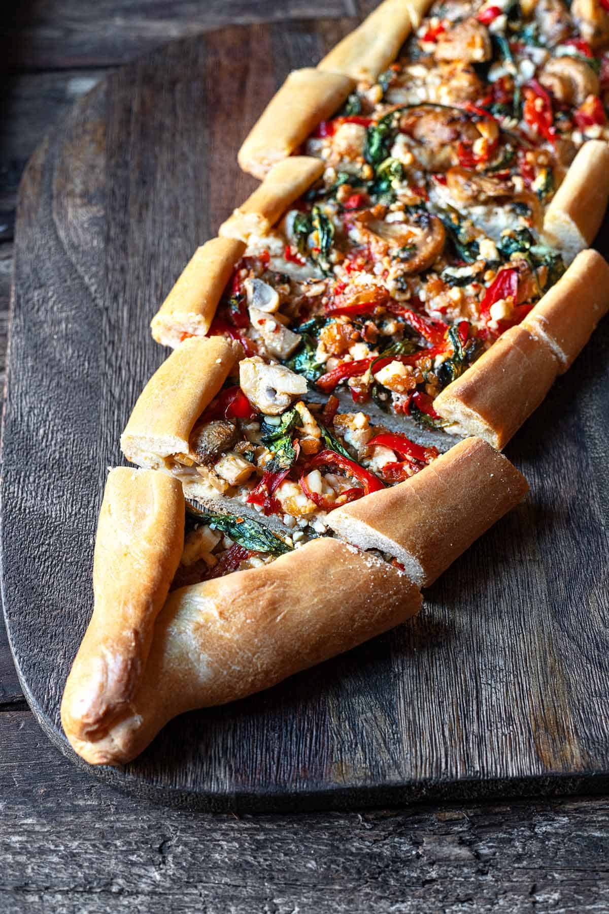one vegetarian turkish pide sliced on a serving board.
