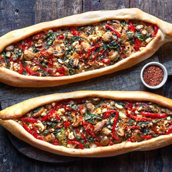 Two baked turkish pide on a serving board with a bowl of aleppo pepper.