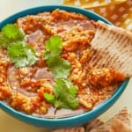 zaalouk (Moroccan cooked eggplant salad) in a blue bowl with a cilantro garnish and a piece of pita bread.