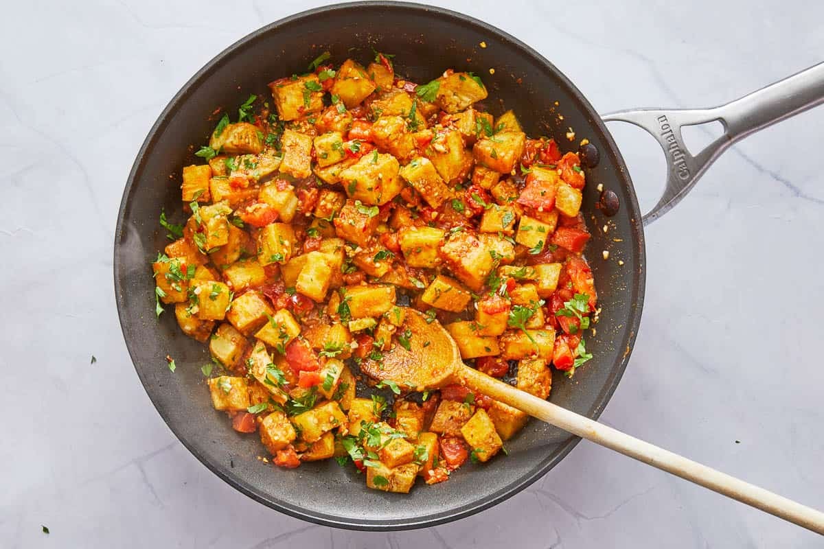 vegetable being sauteed in a frying pan and a wooden spoon.