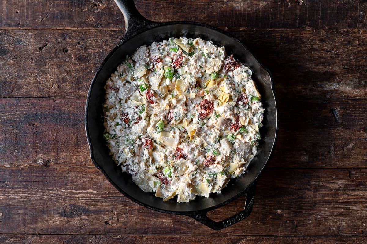 uncooked artichoke dip with feta in a cast iron skillet.