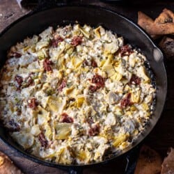 close up of cooked artichoke dip with feta in a cast iron skillet surrounded by fried pita chips.