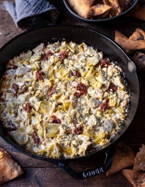 close up of cooked artichoke dip with feta in a cast iron skillet surrounded by fried pita chips.