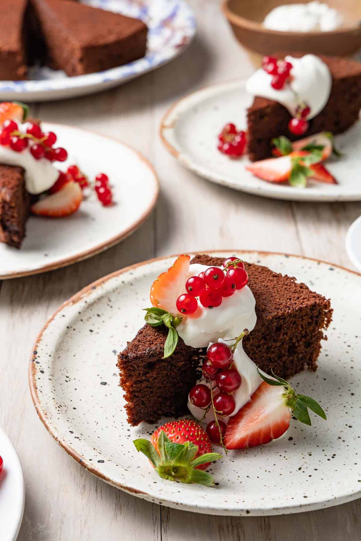 three slices of chocolate olive oil cake topped with greek yogurt whip and berries on three plates.